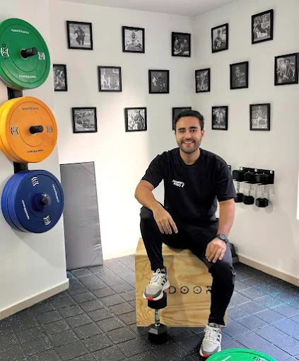 Juanma sentado sobre un cajón de madera en el centro, con discos de colores y fotos enmarcadas en la pared